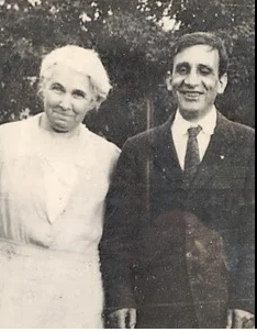 A black and white photo of Francis and Laura Ierardi standing together with trees in the background.  Laura is wearing a light colored dress and Francis is wearing a dark suit.