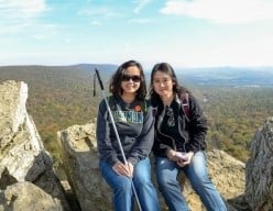 Harriet, cane in hand, and her sister Heather of team H&H go sitting at the top of a mountain trail with a view of a valley behind them.