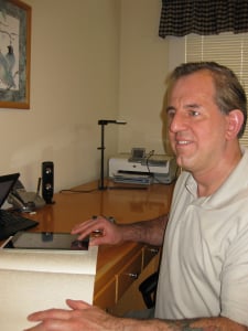 Larry Lewis, author of iOS Success, sitting at his desk with a copy of the book and an iPad